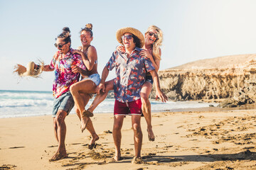 Group of people young friends play and have fun together at the beach - summer holiday vacation tourists - ocean and sky in background - men and women laughing and carrying