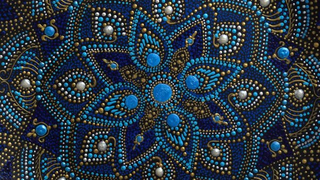 Decorative ceramic plate with black, blue and golden colors, painted plate rotating on background, closeup, top view. Decorative porcelain plate painted with acrylic paints, handwork, dot painting