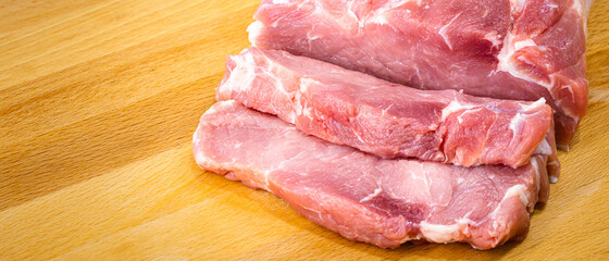 Sliced pieces of raw red pork meat on the wooden cutting board. Food close-up object photo. Studio shot.