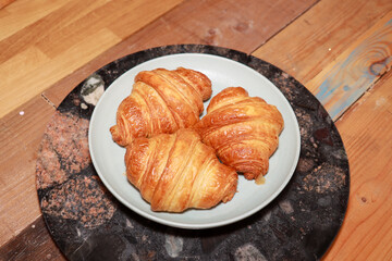 A plate of three freshly made croissants on a plate in a kitchen on a wooden work top