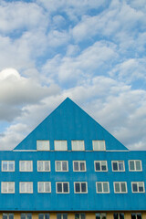 Blue building with a triangular roof and windows. Against the background of the sky..