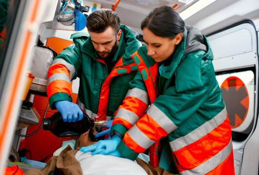 Two paramedics are resuscitating a senior lying on a gurney in an ambulance by performing chest compressions and connecting to a ventilator.