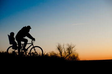 A silhouette of a father and his child ona bicycle during the sunset.