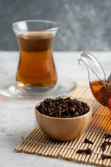 A glass cup of tea with dried cloves and teapot