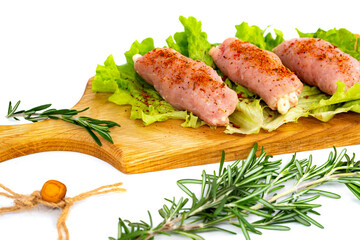 Pieces of meat lie on a cutting board with herbs and rosemary. Semi-finished meat products