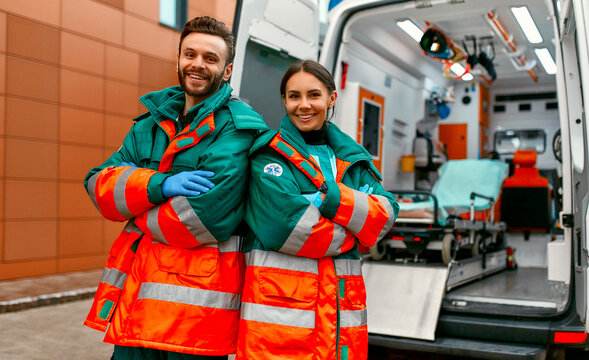 Two paramedics in uniforms stand with their arms crossed in front of a clinic and a modern ambulance.