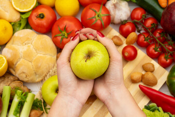 A girl holding a green apple in her hands on a table with vegetables