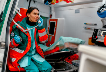 Beautiful woman paramedic in uniform answers the phone call while sitting in a modern ambulance car.