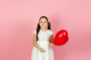 Obraz na płótnie Canvas close-up joyful girl in white dress holding red heart shaped balloon on valentine's day isolated on pink background.