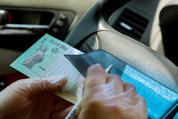 Obraz premium Writing on blank check to in car with gloves on depositing government stimulus check with gloves on for safety