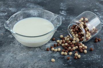 Glass jar of cereal balls and milk on marble background