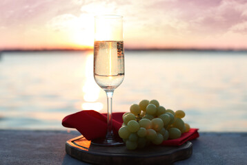 Glass of champagne and and fresh grapes served near river at sunset