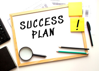 SUCCESS PLAN text is written on a white office board. Work table with office supplies.