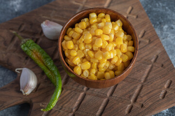 Bowl of canned corn, garlic and pepper on wooden board