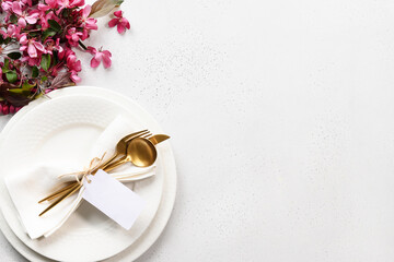 Spring elegance table setting with apple tree flowers, golden cutlery and tag on white table. View...