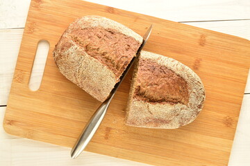 Two halves of a loaf, fragrant buckwheat bread with a metal knife on a wooden cutting board, close-up, on a wooden table.