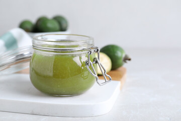 Feijoa jam in glass jar on light grey table, closeup. Space for text