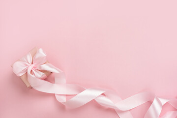 Gift box with long ribbon on pastel pink background. Present for Valentines Day, Mother's Day or Women's Day. Festive monochrome background. Top view flat lay with free space.