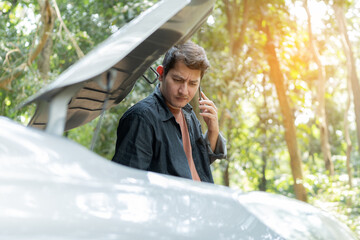 Man using phone for repair as maintenance service. Man trying to repair a car engine, looking inside open bonnet