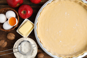 Raw dough and ingredients for traditional English apple pie on wooden table, flat lay