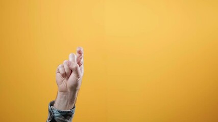 A male's hand waves her hand in a gesture of farewell. Yellow background. The concept of gestures