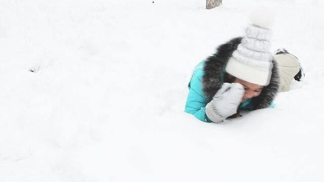 Closeup view of cute girl playing happily in white fluffy fresh snow outdoor in winter. Laying on th snow and smiling.