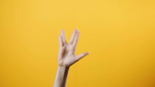 A female hand appears from below with a fist gesture, and then makes a vulcan greeting gesture. Yellow background. The concept of gestures