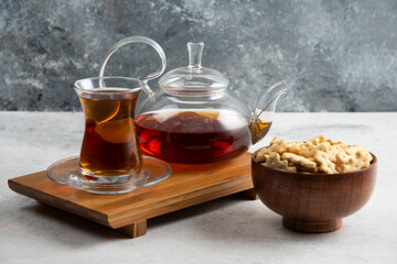A glass cup of tea with wooden bowl full of crackers