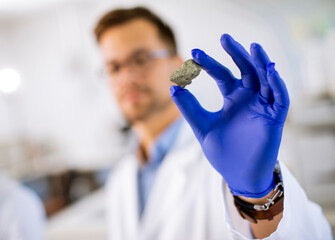 Young scientist hold a mineral specimen in protective glove at material science lab