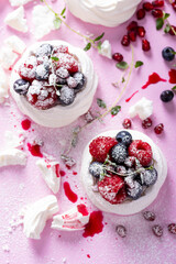 Pavlova meringue cake with cream and berries on dusted sugar pink background