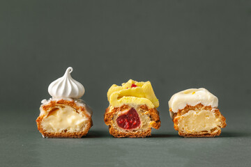 Set of fresh eclairs cut with  butter cream filling and meringue cookies decoration. French pastry on the dark green or grey background.