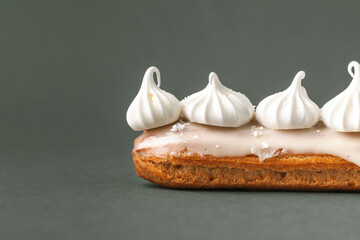 Fresh eclair with  butter cream filling and meringue cookies decoration. French pastry on the dark green or grey background. Macro shot - obrazy, fototapety, plakaty