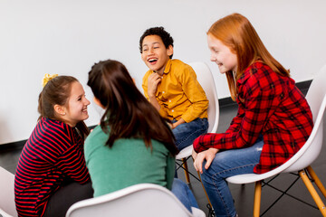 Portrait of cute little kids in jeans  talking and sitting in chairs against white wall