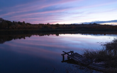 закат над рекой, небо отражается в воде, на берегу реки небольшой мостик