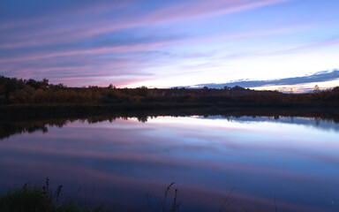 sunset over the river, the sky is reflected in the water, there is a small bridge on the river bank