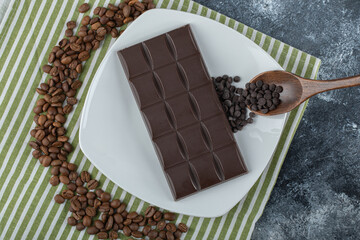 Bar of chocolate with coffee beans on a tablecloth