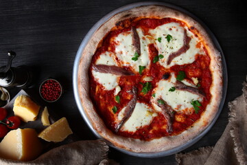 Pizza with anchovies. Traditional Italian pizza. Metal plate for serving pizza. A piece of parmesan cheese and other ingredients on a dark background. The view from the top.