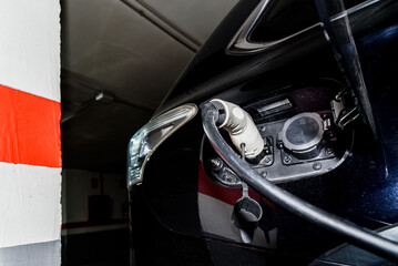 A car recharges its electric batteries inside a private garage with its own charging station, detail of the connected plug.