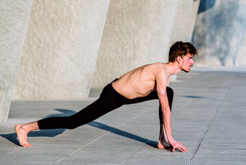 Young red-haired male athlete performing stretching after training to gain flexibility and relax his muscles, outdoors with unfocused background.