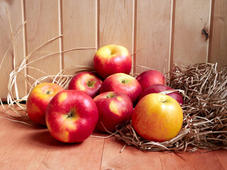 Bright red and yellow apples are stored in hay on a wooden surface