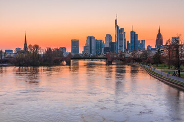 Fototapeta na wymiar Frankfurt skyline in the evening. Sunset over the river Main from the city center. Building of the financial and business district. Park along the bank with trees and meadow