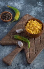 Bowl of sweet corn, garlic and pepper on wooden board