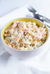 White plate with olivier salad and cutlery on a table with a light fabric tablecloth, New Year's holidays. 