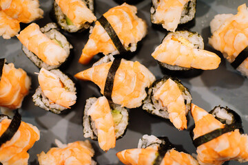 Black plate full of sushi with prawns on top.