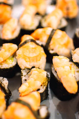 Black plate full of sushi with prawns on top.