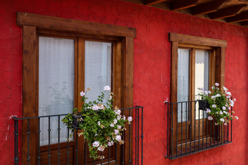 Balcón tipico de la Rioja con flores sobre una pared y ventanas de madera con cortinas