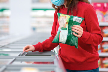 Antiviral protection in public places. A woman in a medical mask buys frozen food in a supermarket....