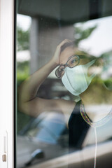 Women wearing a face mask looking outside and felt bored staying at home