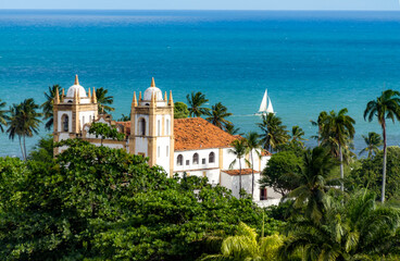 View of the Igreja do Carmo de Olinda - Mount Carmel Chruch, Olinda, Pernambuco, with the sea and a sailboat in the background. - obrazy, fototapety, plakaty