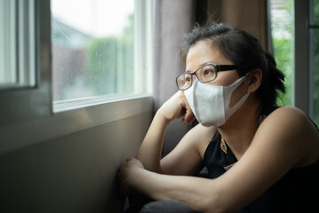 Women wearing a face mask sitting on the sofa and look outside felt bored staying at home